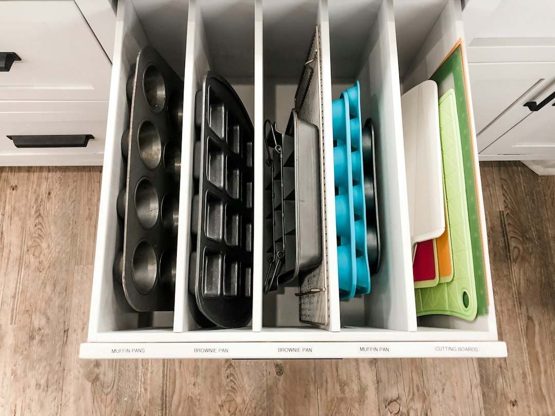 A kitchen drawer with vertical dividers organizing baking pans and colorful cutting boards