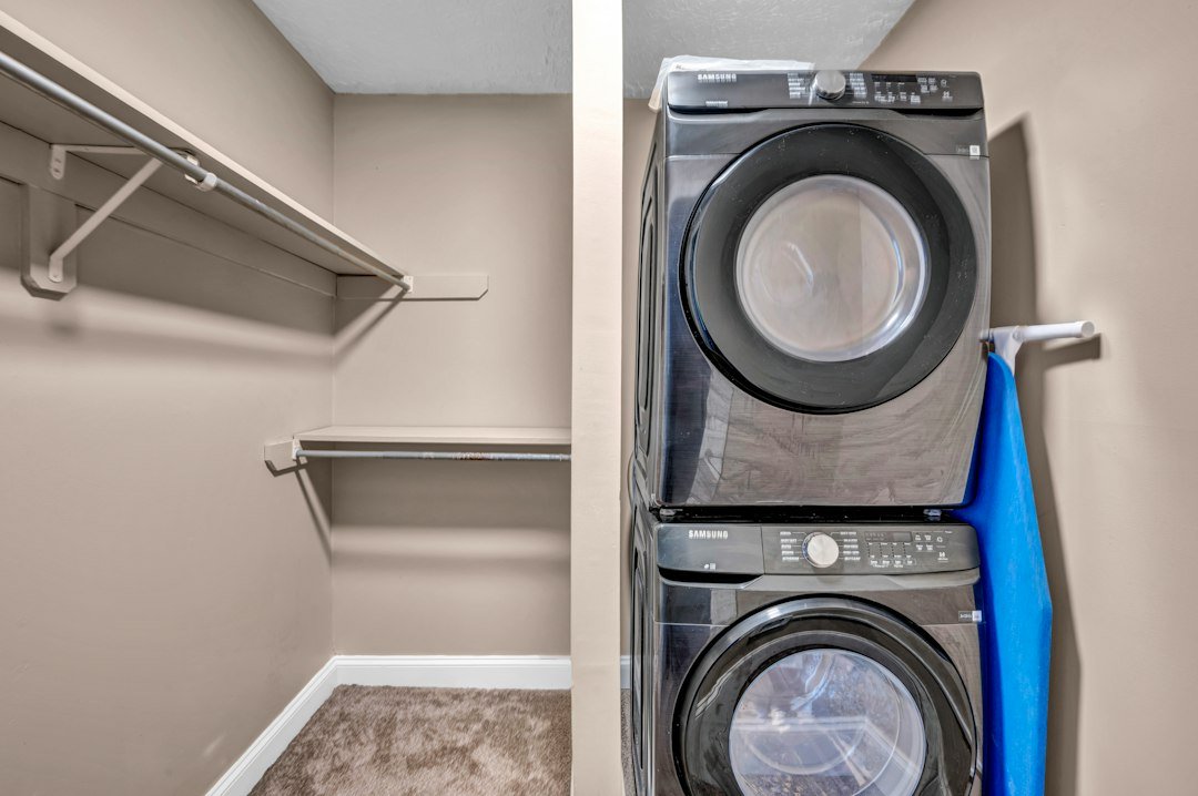 A stacked washer and dryer in a closet with beige walls and shelving